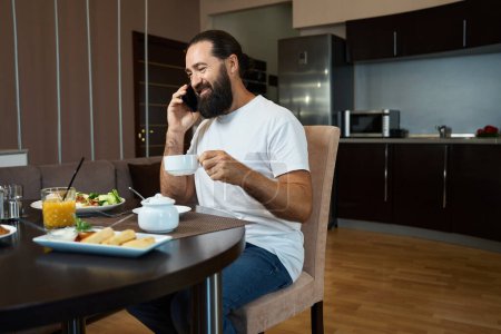 Foto de Hombre de negocios de mediana edad hablando por teléfono en el desayuno, platos con comida en la mesa - Imagen libre de derechos