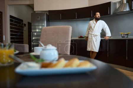 Téléchargez les photos : Invité de l'hôtel dans un peignoir profite de la matinée dans la chambre d'hôtel, petit déjeuner et café du matin sur la table - en image libre de droit