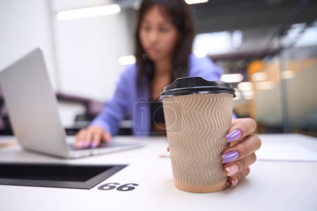 Foto de Trabajadora sosteniendo taza de café sobre fondo borroso de oficina de espacio abierto - Imagen libre de derechos