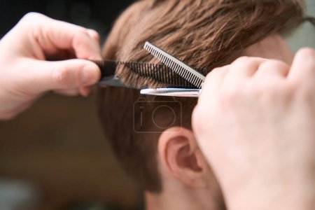Foto de Vista de cerca en las manos de la peluquería cortar el pelo del visitante mediante el uso de tijeras y peine en el interior - Imagen libre de derechos