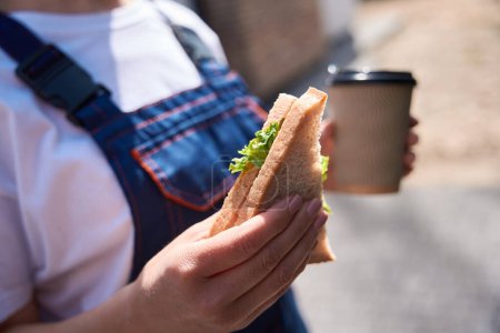 Photo for Woman building engineer has lunch break, eating sandwich and drinking coffee, spending time at construction site, healthy snack, close-up - Royalty Free Image