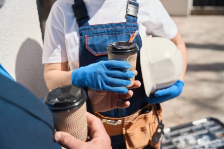 Téléchargez les photos : Ingénieur constructeur femme prenant le café que le contremaître lui apporte, collègues discutant du processus de construction et profitant de boissons en plein air - en image libre de droit