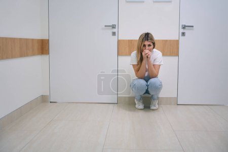 Photo for Female blonde woman in jeans is squatting in the hospital corridor, the woman is very upset - Royalty Free Image