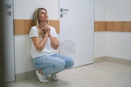 Foto de Mujer joven en jeans está en cuclillas en un pasillo del hospital, la mujer está muy molesta - Imagen libre de derechos