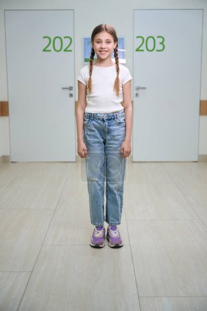 Photo for Smiling girl with pigtails stands in a hospital corridor, she is in comfortable casual clothes - Royalty Free Image