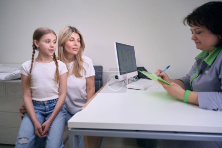 Téléchargez les photos : Maman et fille au rendez-vous avec un allergologue pédiatrique, le médecin signe les papiers médicaux - en image libre de droit