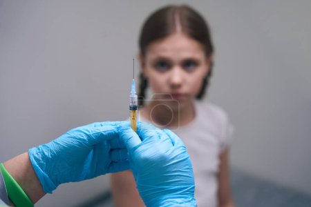 Photo for Nurse in protective gloves holds a syringe with medicine in her hands, next to a girl with pigtails - Royalty Free Image