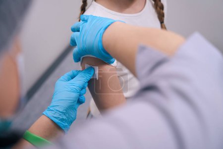 Photo for Nurse glues a patch after an injection on a girls hand, a health worker in protective gloves - Royalty Free Image