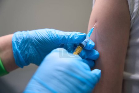 Foto de Paciente en la clínica recibe una vacuna preventiva en el brazo, el médico utiliza una aguja delgada - Imagen libre de derechos