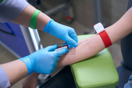 Téléchargez les photos : Infirmière dans des gants de protection prend le sang pour l'analyse d'un patient, un médecin utilise des matériaux stériles - en image libre de droit