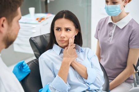 Photo for Anxious woman stomatologist client complaining to doctor on sharp and sudden pain in her teeth, wear away of enamel, dental infection, nerve inflammation - Royalty Free Image