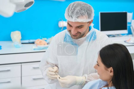 Foto de Ortodoncista altamente calificado explicando al proceso de tratamiento de dientes de cliente femenino, mostrando herramienta dental especial y funciona, servicio clínico privado, odontología estética - Imagen libre de derechos