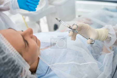 Foto de El paciente joven se encuentra en una silla dental, el médico sostiene una jeringa con analgésicos en las manos - Imagen libre de derechos