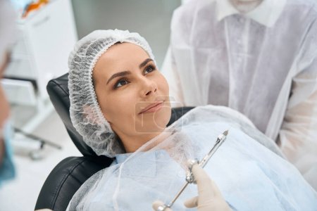 Foto de Hermosa hembra se encuentra en una silla dental, el médico tiene una jeringa con analgésicos en las manos - Imagen libre de derechos