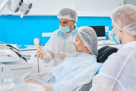 Foto de Doctor y su asistente trabajan en el consultorio dental, el paciente se encuentra en la silla dental - Imagen libre de derechos