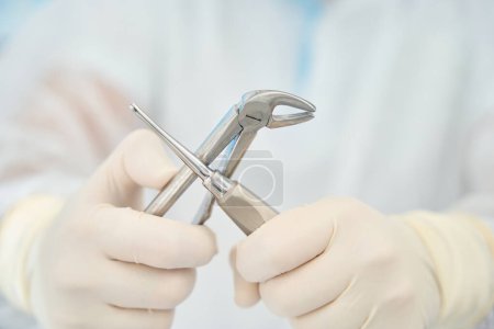 Téléchargez les photos : Dentiste tient dans sa main un outil spécial pour enlever les dents, les dispositifs sont en acier médical - en image libre de droit