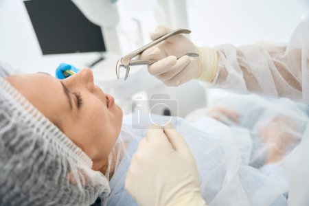 Foto de Paciente femenina joven en una silla dental en una extracción dental, el dentista utiliza fórceps especiales - Imagen libre de derechos