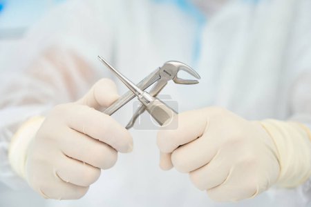 Téléchargez les photos : Homme tient dans sa main des instruments dentaires spéciaux pour l'extraction des dents, les dispositifs sont en acier médical - en image libre de droit