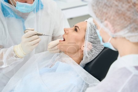 Téléchargez les photos : Jeune patiente à un rendez-vous chez le médecin dans une chaise dentaire, le dentiste utilise des outils spéciaux - en image libre de droit