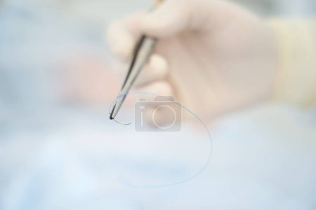 Foto de Cirujano sostiene en su mano una aguja quirúrgica y material para suturar una herida postoperatoria - Imagen libre de derechos