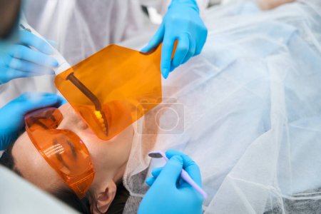 Foto de Dentista pone un relleno de fotopolímero en el paciente, el asistente utiliza una pantalla protectora - Imagen libre de derechos