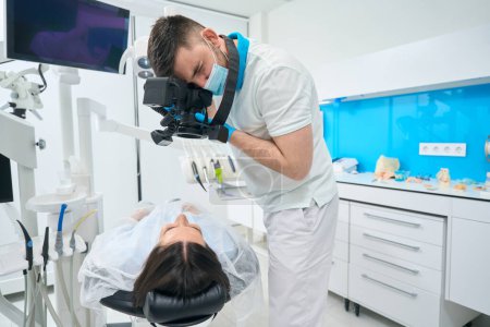 Foto de Mujer morena se encuentra en una silla dental, el médico fotografía sus dientes con una cámara - Imagen libre de derechos