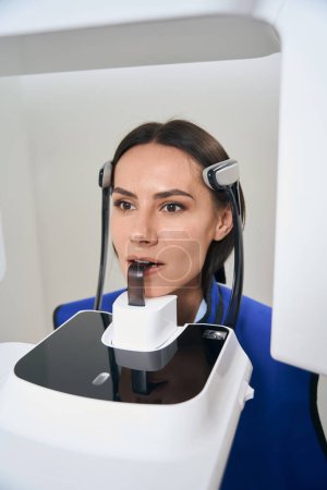 Foto de Encantadora dama se somete a procedimientos de escaneo 3D en equipos modernos, un paciente en un delantal de protección - Imagen libre de derechos