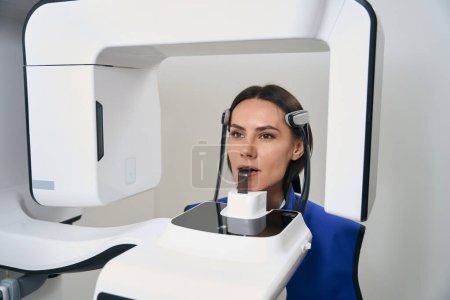 Foto de Hermosa dama se somete a procedimientos de diagnóstico escaneo 3D en equipos modernos, un paciente en un delantal de protección - Imagen libre de derechos