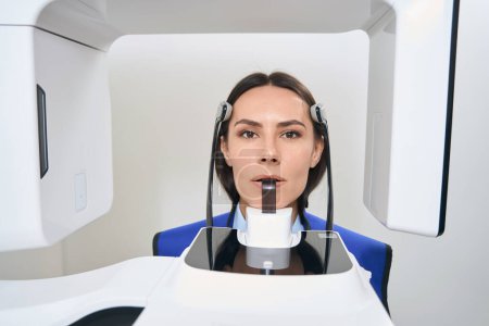 Foto de Paciente morena se somete a procedimientos de diagnóstico escaneo 3D en equipos modernos, una mujer en un delantal de protección - Imagen libre de derechos