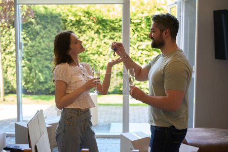 Foto de Hombre guapo sosteniendo vidrio y dando llaves a su mujer que sostiene el vino en el interior - Imagen libre de derechos