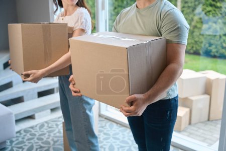 Téléchargez les photos : Vue recadrée de jeune homme et femme en vêtements décontractés apportant des boîtes en carton à la maison - en image libre de droit