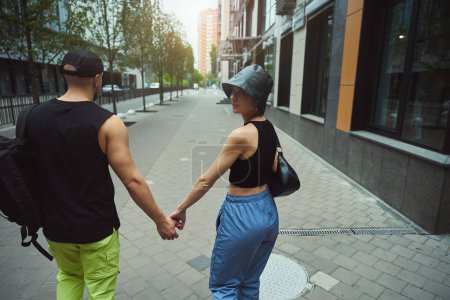 Téléchargez les photos : Jeune femme tourné vers la caméra tout en marchant dans la rue avec son petit ami - en image libre de droit