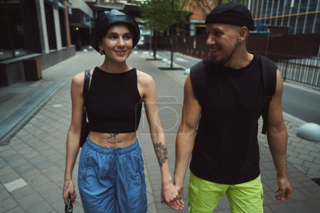 Téléchargez les photos : Joyeux homme et femme en vêtements fantaisie se tenant la main tout en marchant dans la rue - en image libre de droit