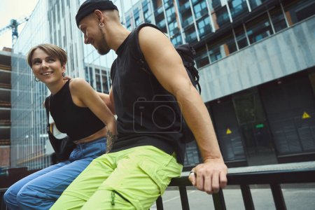 Téléchargez les photos : Homme joyeux montrant l'amour à sa petite amie tout en étant assis sur la rampe à l'extérieur - en image libre de droit