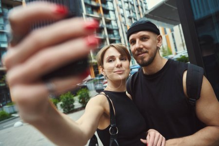 Téléchargez les photos : Jeune femme et homme faisant selfie en utilisant un téléphone portable tout en se tenant à l'extérieur - en image libre de droit