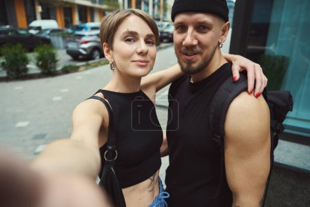 Téléchargez les photos : Selfie de beau couple portant des vêtements à la mode debout dans la rue moderne - en image libre de droit