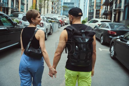 Téléchargez les photos : Vue arrière de l'homme et de la femme caucasiens se tenant la main tout en marchant dans la rue - en image libre de droit
