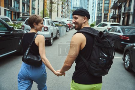 Foto de Vista trasera del hombre y la mujer sonrientes tomados de la mano mientras caminan afuera - Imagen libre de derechos