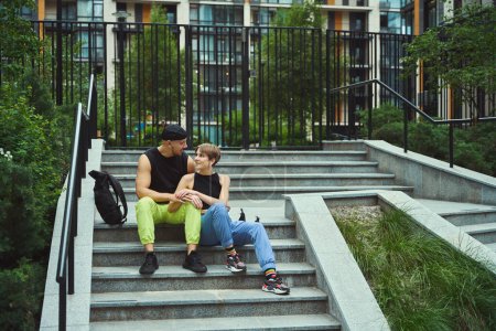 Téléchargez les photos : Blanc homme et femme montrant de l'affection les uns pour les autres tout en étant assis sur les escaliers à l'extérieur - en image libre de droit