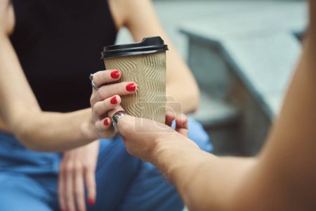 Téléchargez les photos : Vue recadrée des mains de la femme avec manucure rouge tenant tasse de café dans la zone urbaine - en image libre de droit
