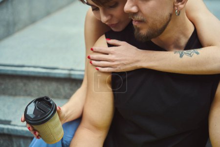 Téléchargez les photos : Vue recadrée de la jeune femme avec tasse de café embrassant son petit ami tout en étant assis sur les escaliers - en image libre de droit