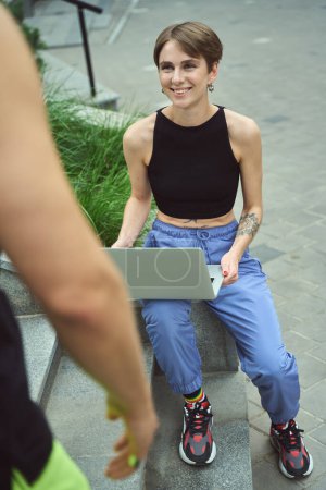 Photo for Attractive female with happy facial expression looking at her boyfriend while sitting in urban environment - Royalty Free Image