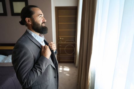 Photo for Hotel guest admires the view from the window of the hotel room, there is a large bed in the room - Royalty Free Image