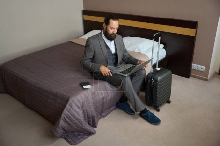Foto de Viajando hombre de negocios se sentó con el ordenador portátil en la cama para descansar de la carretera, junto a su pasaporte y billete - Imagen libre de derechos