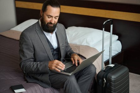Foto de Hombre viajero se sentó con un portátil en la cama, junto a su pasaporte y billete - Imagen libre de derechos