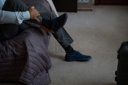 Téléchargez les photos : Voyageur fatigué enlève ses chaussures de la route, il est situé sur un grand lit - en image libre de droit