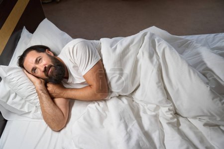 Foto de Hombre despertado toma el sol en una cama grande, él es un huésped de un hotel cómodo - Imagen libre de derechos