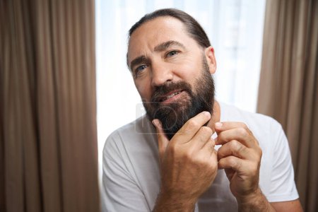 Foto de Varón de mediana edad examina su barba gruesa, un hombre con ropa blanca - Imagen libre de derechos
