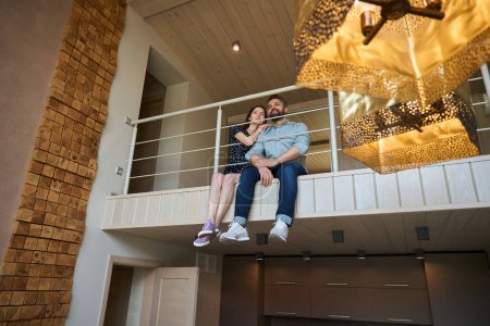 Téléchargez les photos : Couple d'âge moyen est assis sur le palier au deuxième étage de leur maison, l'intérieur utilise des matériaux respectueux de l'environnement - en image libre de droit