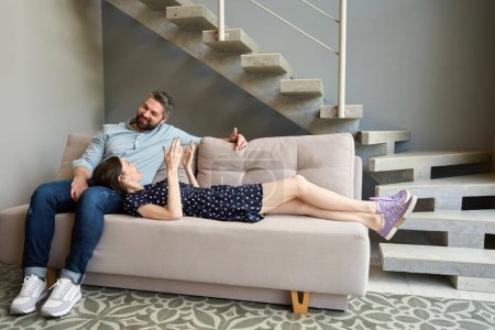 Téléchargez les photos : Homme et femme communiquent chaleureusement sur un canapé moelleux, une femme s'allonge sur les genoux de son mari - en image libre de droit